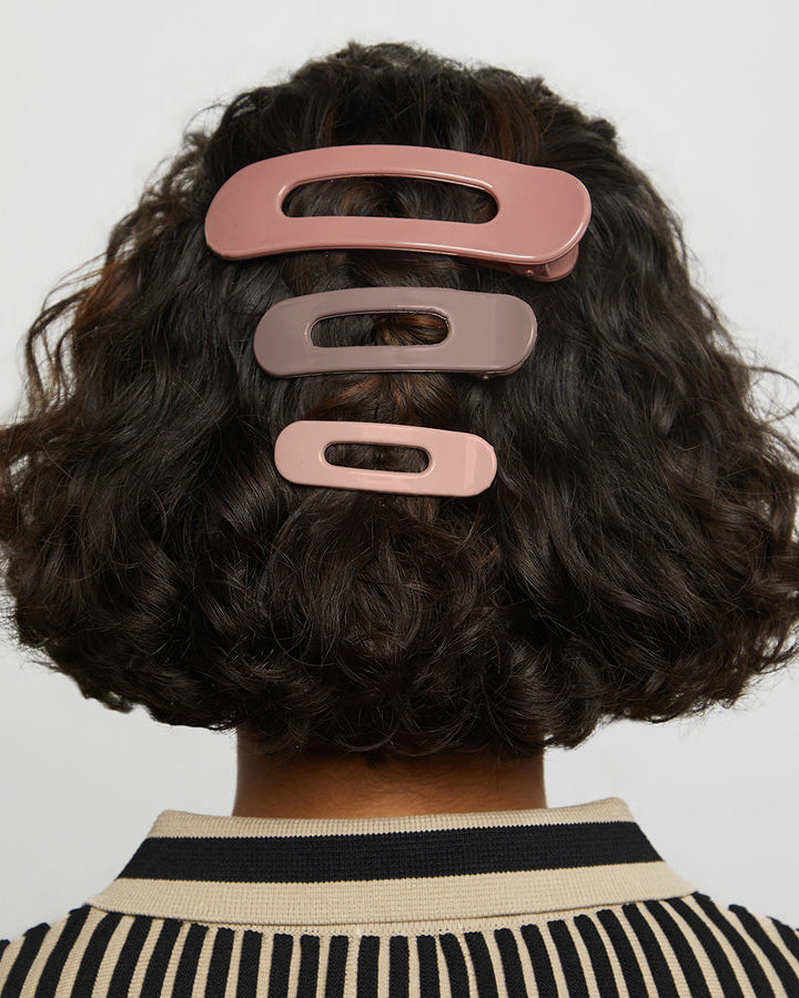Person with three different sized pink and brown neutral hued flat hair clips in their hair.