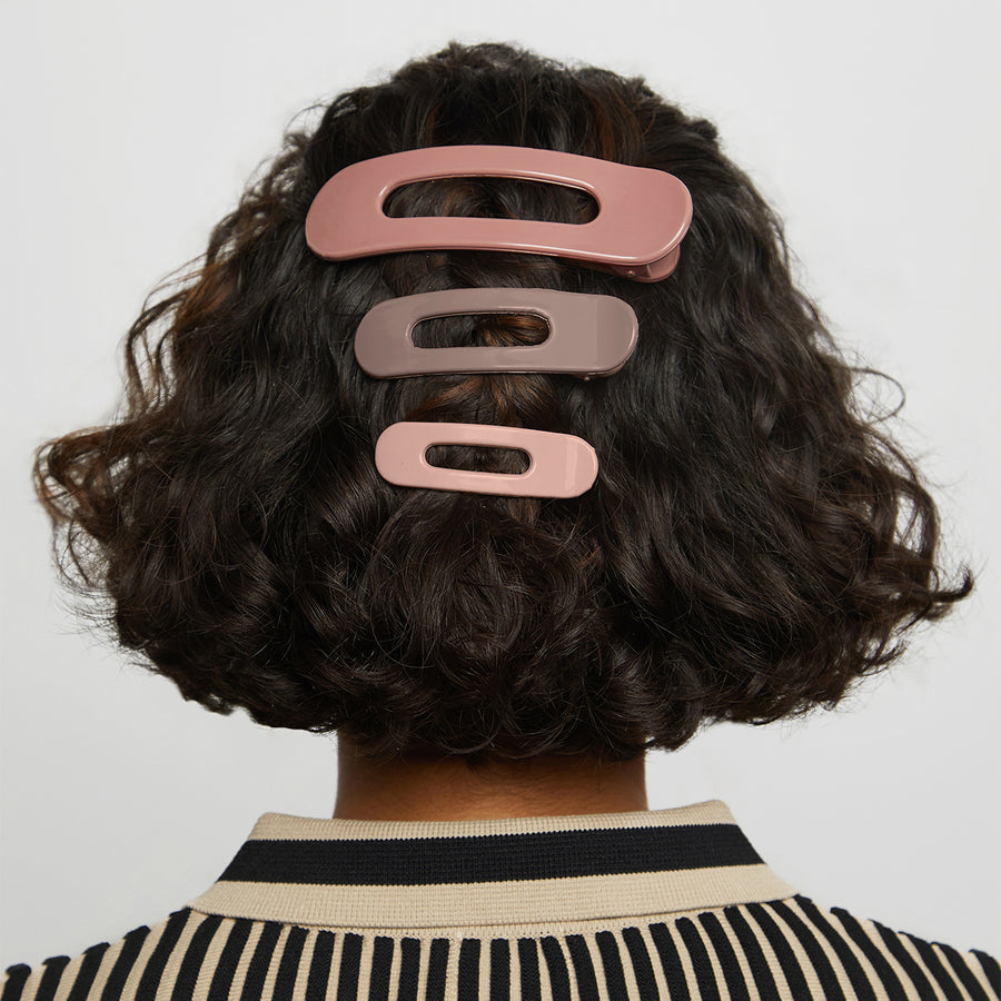 Person with three different sized pink and brown neutral hued flat hair clips in their hair.